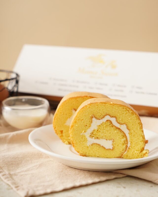 Irisan Bolu Gulung Original Mama Swan dengan isian krim, di depan kotak kemasan